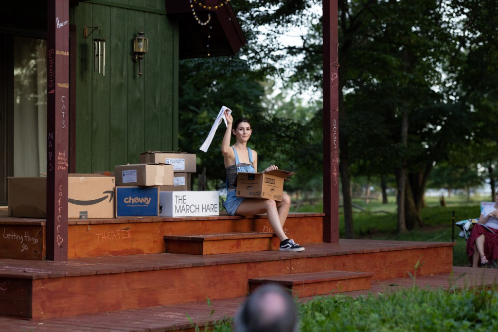 Katie sits on stage. She waves a sleeve, which she has pulled from the box on her lap.